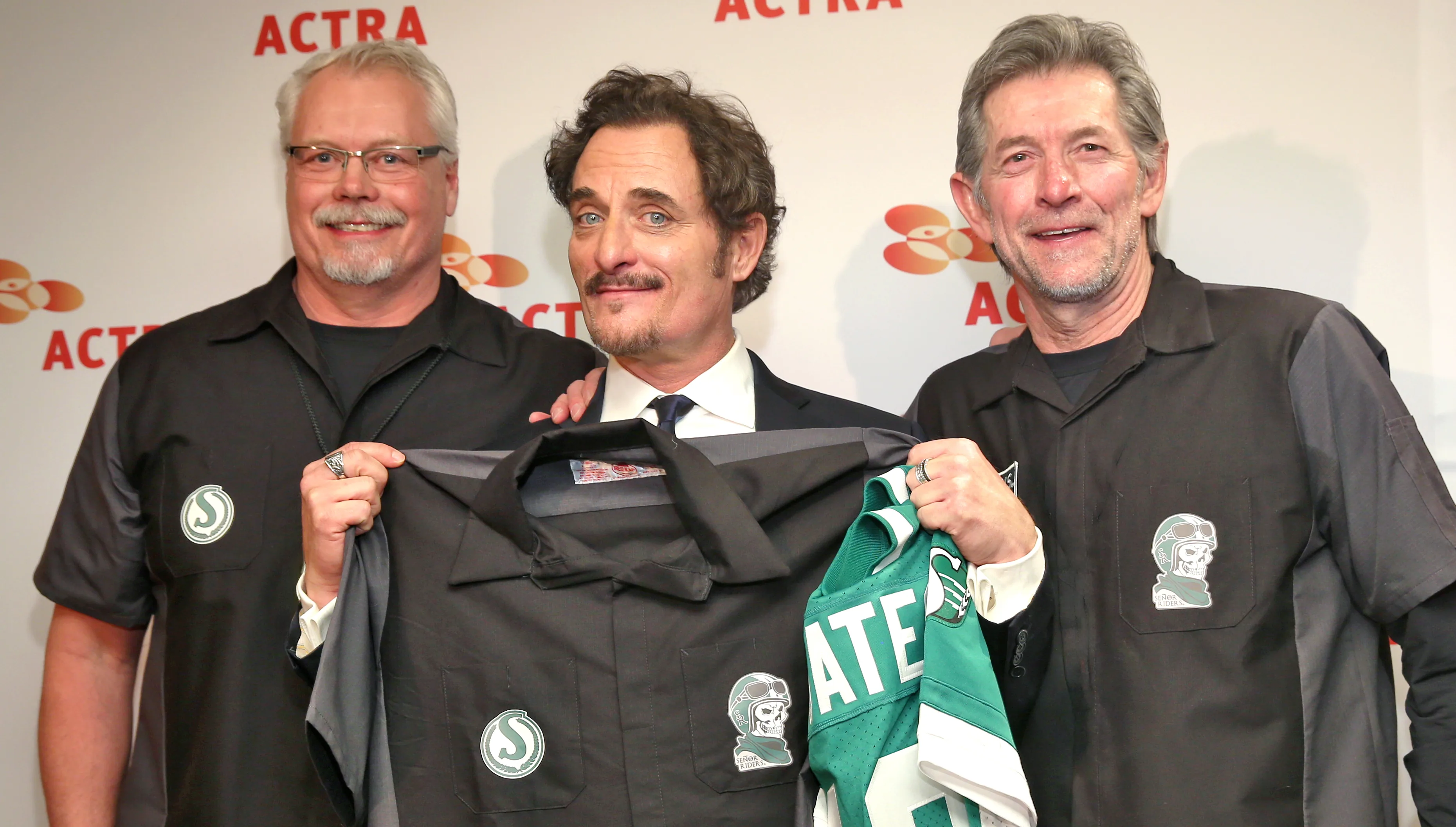 Saskatchewan Roughriders alumni Al Johns 1980–1987 Defensive Tackle and Steve Mazurak 1973–1981 Wide Receiver present honorary jerseys to Kim during the 2017 ACTRA National Award of Excellence celebration at the Beverly Hilton in Los Angeles.